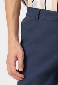 Navy blue pants made of smooth fabric, featuring a flat front and tailored fit. Includes a standard waistband with a belt loop.