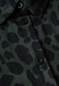 Grønne stoffer med et sort leopardprint mønster, der har knapdetalje og krave, fremhæver en blød tekstur og et casual design.