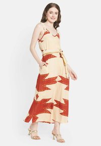 Robe maxi avec une base beige ornée de motifs géométriques rouges et de accents jaunes, ceinture en tissu et poches latérales ; matériau léger.
