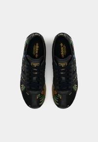 Svarta lädersneakers med blommig broderi i grönt, orange och blått, med tre svarta ränder och en gul logo på tungan.
