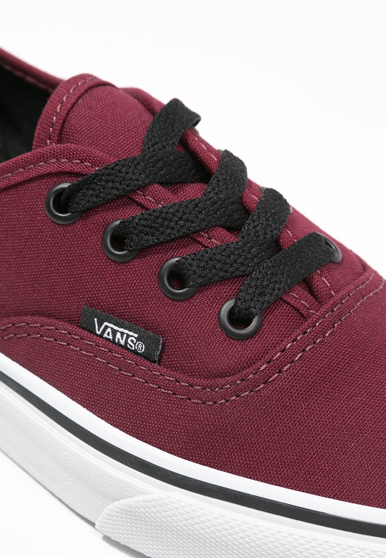 Zapatillas de lona burdeos con cordones negros, ojales reforzados, suela de goma blanca y un logo "VANS" negro en el lateral. Diseño simple y clásico.