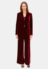 Bordowy aksamitny garnitur z dopasowaną marynarką z klapami notch, dwoma kieszeniami oraz szerokimi spodniami o gładkiej fakturze.