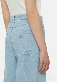 Světle modré denimové džíny s vysokým pasem, velkými zadními kapsami, logem na pravé kapse a jemnými detaily prošití.