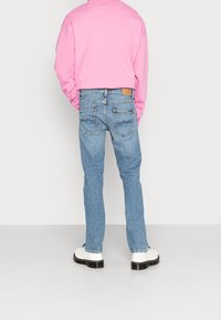 Ljust blå denimjeans med rak skärning, med två bakfickor med dekorativ sömnad och en brun läderlapp vid midjan.