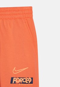 Orange sweatpants made of soft fabric, featuring side pockets and an elastic waistband. Includes a Nike logo and graphic text detail.