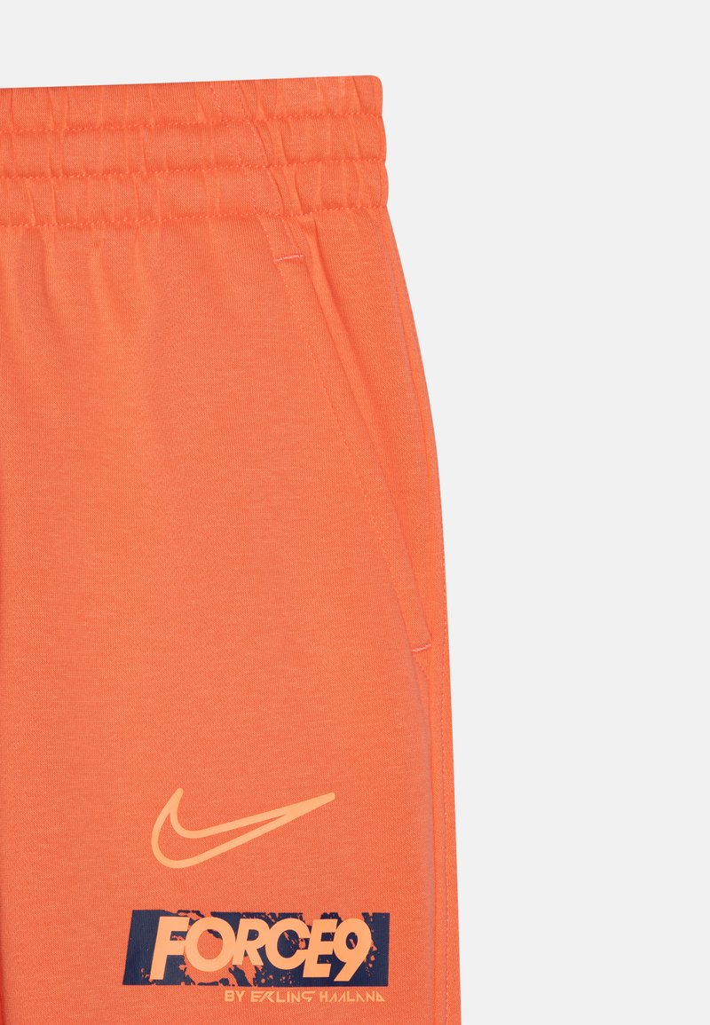 Pantaloni della tuta arancioni realizzati in tessuto morbido, con tasche laterali e vita elasticizzata. Include un logo Nike e dettagli di testo grafico.