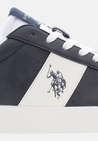 Pánské tenisky s horní částí z modré a bílé kůže, bílými tkaničkami a grafikou jezdců na boku. Texturovaná podešev pro lepší přilnavost.