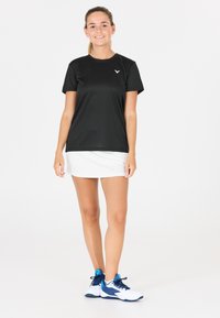 Sort atletisk T-shirt, hvid nederdel og blå/hvide sneakers. Korte ærmer, blødt stof, enkelt design og ingen synlige mønstre eller accenter.