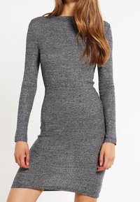 Grått stickat klänning med långa ärmar, figurnära design, strukturerad tyg och en rund halsringning, som når ovanför knäet.