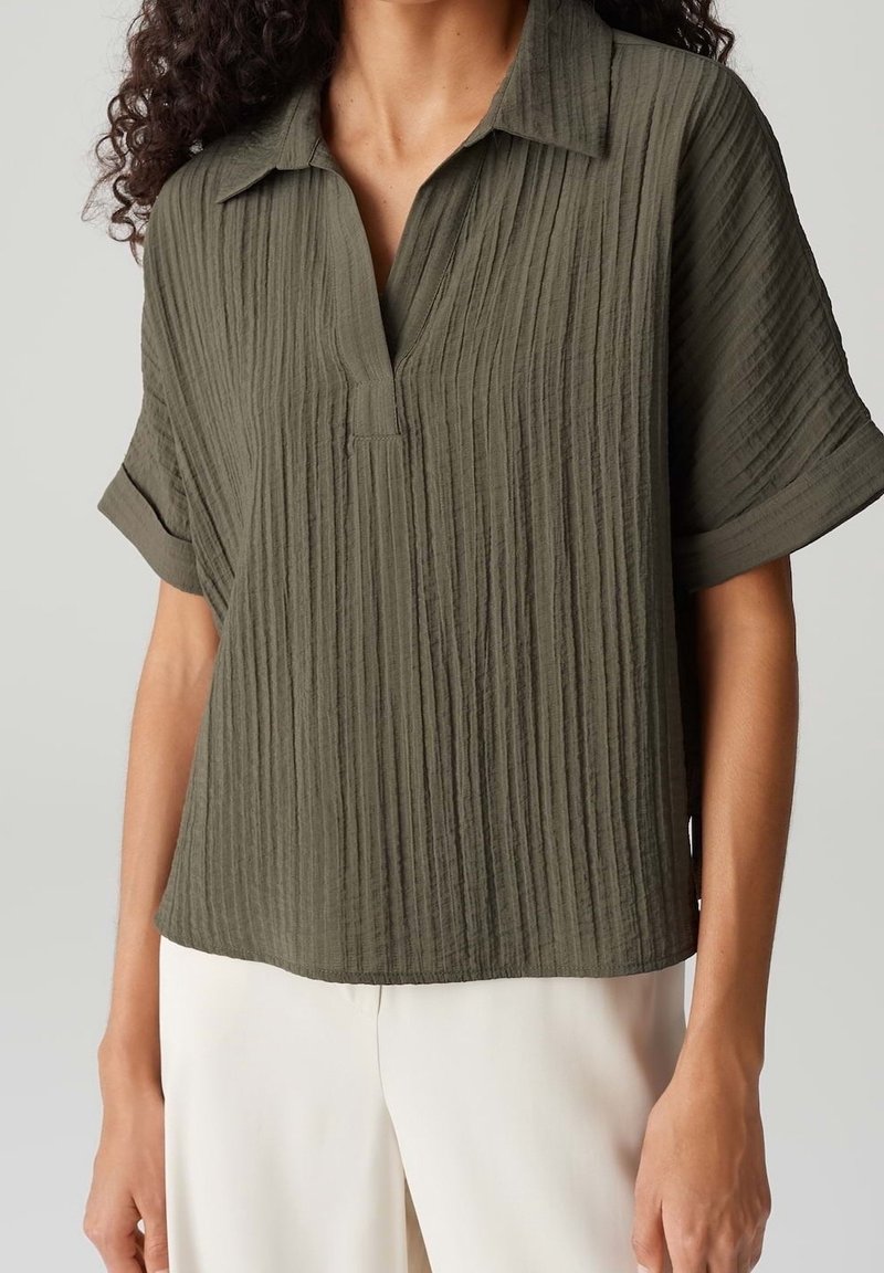 Chemise olive verte à manches courtes avec un col en V, dotée d'un tissu texturé et plissé, et d'une coupe décontractée.