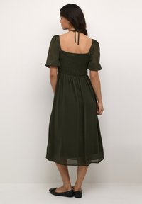 Rochie midi verde măsliniu cu mâneci bufante, cu corset pliat și o curea la spate, având o fustă fluidă și o țesătură ușoară.