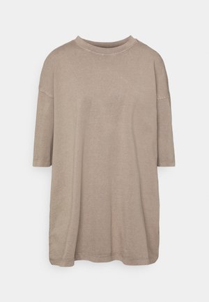 Przestronna koszulka z krótkim rękawem w beżowym kolorze, wykonana z bawełny, z okrągłym dekoltem i miękką teksturą, ozdobiona przeszyciami wzdłuż krawędzi.