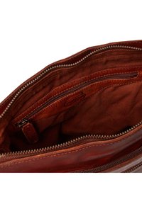 Interno di una borsa in pelle marrone con una superficie liscia, dotata di una tasca con zip e una fodera morbida, evidenziando i dettagli delle cuciture e della cerniera.