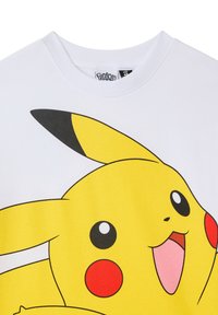 T-shirt in cotone bianco con una grande grafica di Pikachu gialla, con dettagli neri e guance rosse. Design a girocollo, texture liscia.