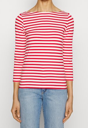 Femme portant un haut cintré à manches longues avec des rayures horizontales rouges et blanches et un jean taille haute bleu clair.