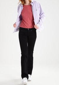 Chaqueta lila, camiseta roja y jeans negros acampanados. Zapatillas blancas completan el atuendo. Diseño y ajuste casual.