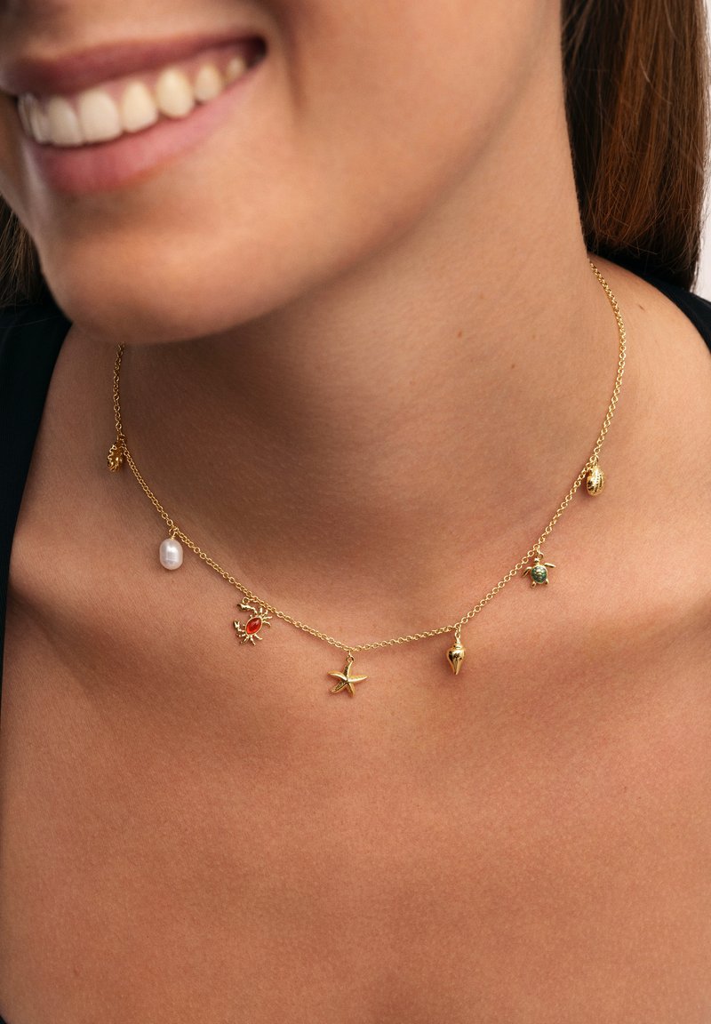 Collier en chaîne en or avec divers pendentifs : un crabe rouge, une étoile de mer, une tortue verte, une coquille de conque, une perle et d'autres accents sur le thème marin.