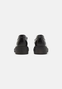 Scarpe in pelle nera con finitura liscia, punta rotonda e dettagli testurizzati sul tallone. Presentano una suola in gomma spessa e leggermente rialzata.