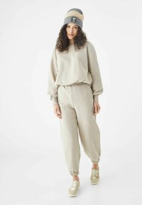 Beige sweatshirt en bijpassende joggers gemaakt van zacht materiaal met geribbelde manchetten. Grijs en beige gestreepte gebreide beanie met logodetail.