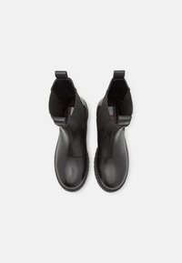 Paire de bottines en cuir noir avec panneaux élastiques sur les côtés et languettes de tirage, vues de dessus sur un fond clair.