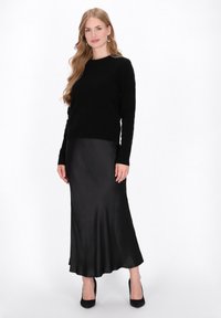 Maglione nero in maglia abbinato a una gonna maxi svasata nera in satin. L'outfit presenta una silhouette classica e texture morbide, completato da scarpe con tacco.