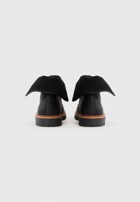 Botas de tobillo de cuero negro con un suave cuello negro, entresuela marrón claro y suela texturizada. Presentan un diseño de puntera redondeada.