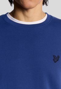Blauwe sweatshirt met een ronde halslijn, voorzien van een witte binnenkraag en een klein zwart logo op de borst. Textuurstof, casual pasvorm.