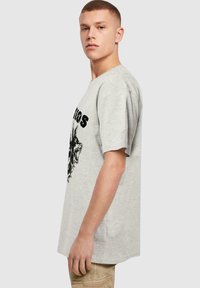 Šedé bavlněné tričko s černým tiskem grafiky vlka na přední straně, krátkými rukávy a volným střihem.