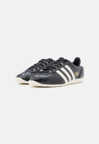 Black sneakers with a textured, shiny surface, featuring three white stripes and a gold "adidas Japan" logo on the side. Rubber sole.