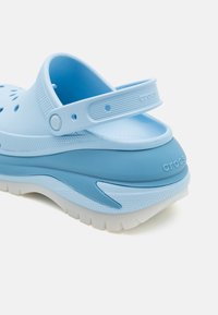 Lyseblå Crocs med en formet design, ventilasjonsåpninger, justerbar bakrem og en teksturert såle med en hvit bunn.