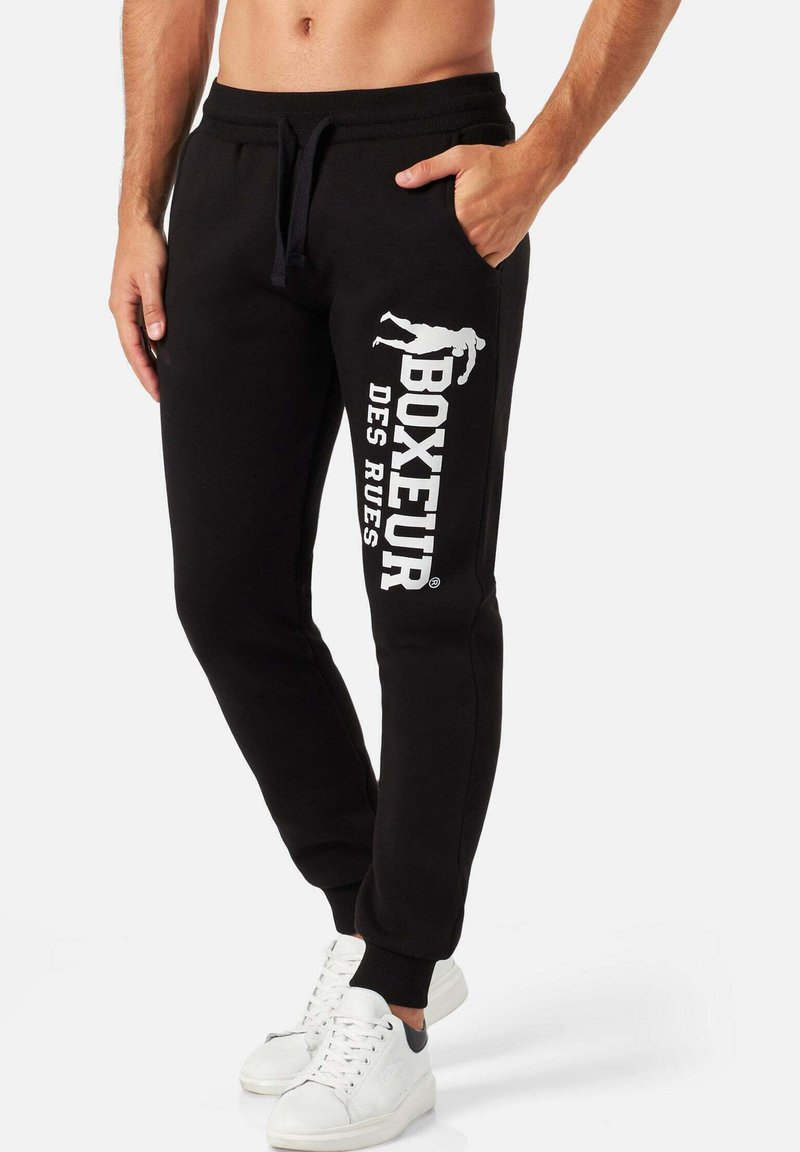 Schwarze Sweatpants aus weichem Material, mit einer Seitentasche und weißem Text mit einem grafischen Design am linken Bein.