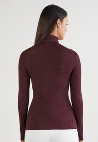 Bordeauxfarbener Langarm-Turtleneck mit einer strukturierten Stoffoberfläche, die Farbtupfer in helleren Tönen aufweist, taillierte Silhouette und hoher Kragen.