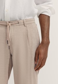 Helle beige Leinenhose mit strukturiertem Finish, ausgestattet mit einem Kordelzugbund und Seitentaschen. Leicht zulaufendes Bein Design.