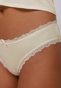 Light beige panties with lace trim along the waistband, featuring a smooth fabric texture and small bow detail at the front.