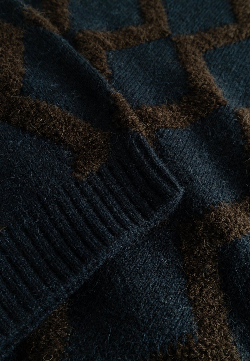 Tissu tricoté bleu foncé avec un motif flou marron. Présente une texture côtelée le long du bord. Matière douce et chaude.