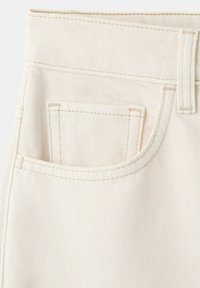 Nahaufnahme einer cremefarbenen Jeanshose aus Denim mit sichtbaren beigen Nähten und einer Gürtelschlaufe oben rechts.