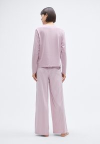 Haut rose à manches longues et pantalon large à rayures, tous deux en tissu doux, avec une coupe décontractée et un léger contraste de couleurs dans le motif.