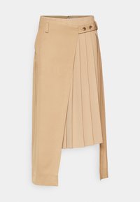 Jupe plissée beige avec un design asymétrique, dotée d'une fermeture à nouer sur le côté et de deux boutons décoratifs à la taille.