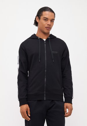 Hoodie noir zippé avec fermeture éclair avant, cordons de serrage et rayures latérales contrastantes arborant un texte logo. Tissu doux, poignets côtelés et ourlet.