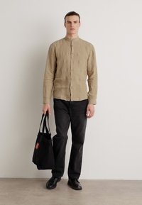 Camisa de lino beige con cuello de banda, botonera en el frente y mangas largas. Combinada con pantalones de mezclilla negros y un bolso negro. Zapatos negros.