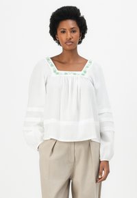 Witte blouse met lange mouwen en vierkante halslijn, voorzien van groene bloemenborduursels, geplooide voorkant en gestreepte mouwen. Gestyled met beige broek.