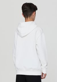 Felpa bianca in cotone con cappuccio regolabile, polsini e orlo a coste. Tessuto morbido, vestibilità rilassata, design minimalista.