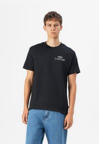 Black cotton t-shirt with a crew neckline and short sleeves. Features a small white embroidered "new balance" logo on the left chest.