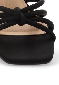 Sandalia negra de tiras con punta cuadrada plana, parte superior de tela suave y plantilla beige lisa con detalles de bandas cruzadas.