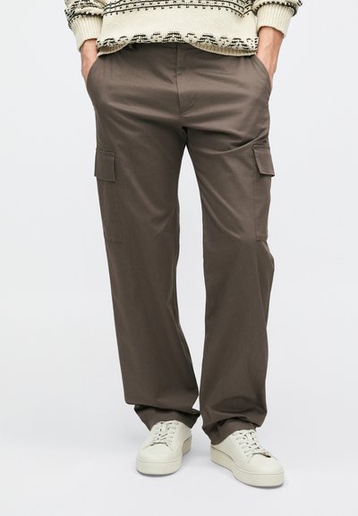 Καφέ cargo παντελόνια με πλαϊνές τσέπες, χαλαρή εφαρμογή, από μίγμα βαμβακιού, σε συνδυασμό με λευκά sneakers. Σχεδιασμένα για πρακτικότητα και άνεση.