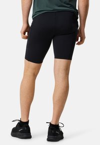Pantaloni sportivi neri realizzati in tessuto elastico, con un design aderente e una texture liscia. Indossati con sneakers nere.