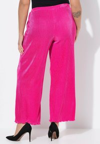 Pantalones de pierna ancha de un vibrante color rosa con una textura acanalada y un detalle de dobladillo con volantes, combinados con zapatos de tacón negro.