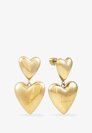 Goldfarbene, herzförmige Ohrringe mit zwei übereinander gestapelten Herzen, die auf dem größeren Herz mit "CPH STUDIOS" graviert sind.