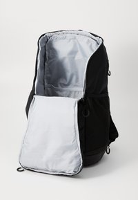 Sac à dos noir avec un intérieur gris, doté d'une grande ouverture, d'une poche latérale en filet et d'un rabat amovible à l'avant pour un stockage supplémentaire.