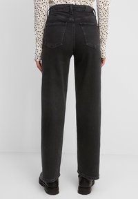 Jeans de mezclilla negros de talle alto con un corte recto, que cuentan con dos bolsillos traseros y detalles de costura sutiles, llevados con una camisa con estampado de puntos.
